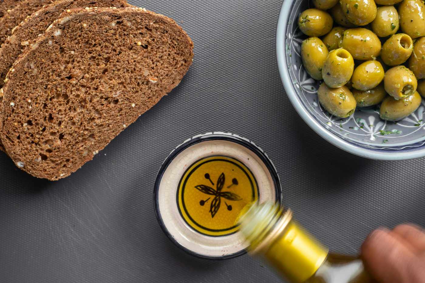 Polyphenolreiches Olivenöl wird über Brot und Oliven gegossen – Longevity-Routine aus der Blue Zone